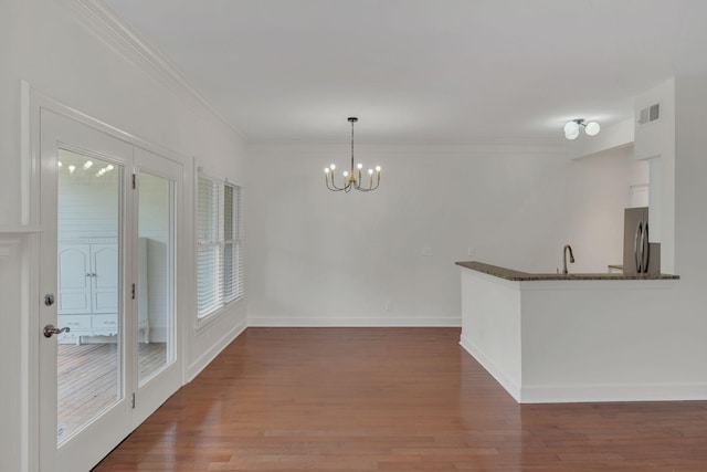 unfurnished dining area featuring a chandelier, wood finished floors, crown molding, baseboards, and a sink