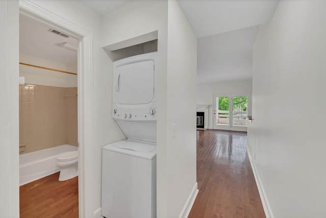 washroom with stacked washing machine and dryer, hardwood / wood-style flooring, and baseboards