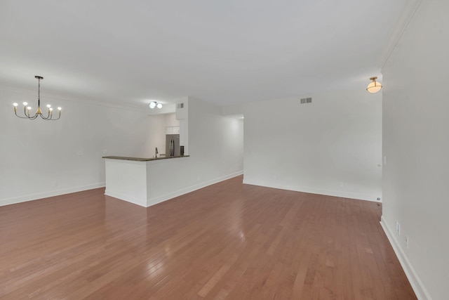 unfurnished living room featuring a chandelier, hardwood / wood-style floors, and baseboards