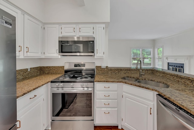 kitchen with stainless steel appliances, a sink, light stone countertops, ornamental molding, and white cabinets