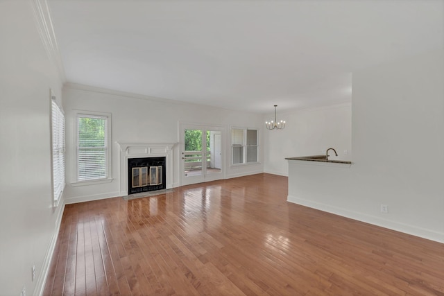 unfurnished living room featuring a chandelier, a premium fireplace, hardwood / wood-style floors, plenty of natural light, and crown molding
