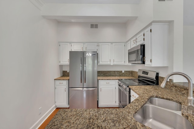 kitchen with appliances with stainless steel finishes, a sink, light stone countertops, wood finished floors, and white cabinetry