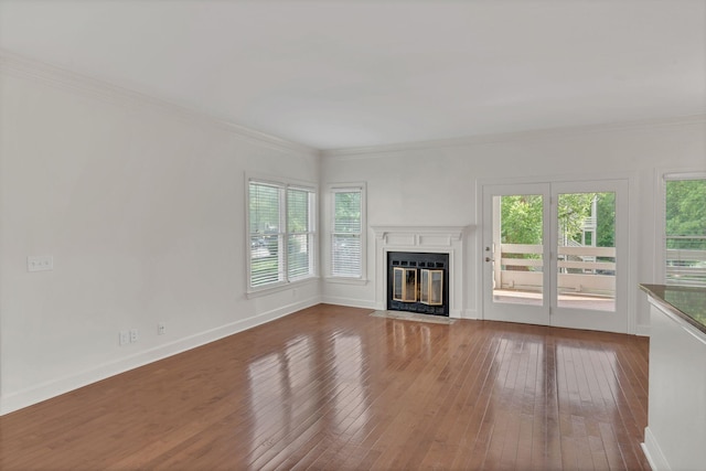 unfurnished living room with healthy amount of natural light, hardwood / wood-style floors, a fireplace with flush hearth, crown molding, and baseboards