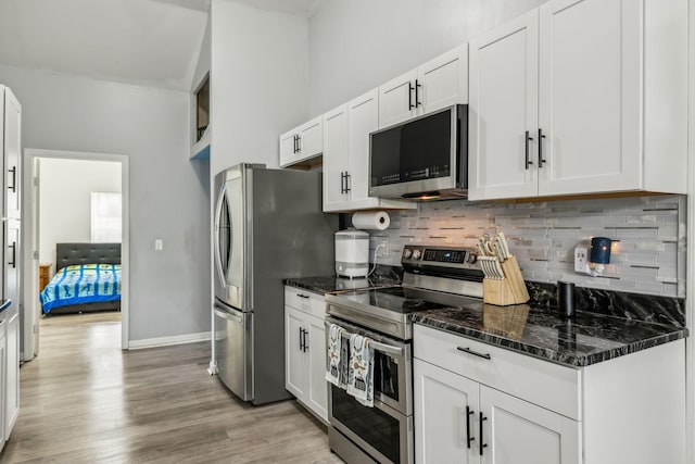 kitchen with stainless steel appliances, white cabinetry, light wood-type flooring, tasteful backsplash, and dark stone countertops