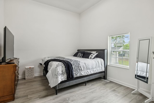 bedroom featuring light wood-type flooring, baseboards, and vaulted ceiling