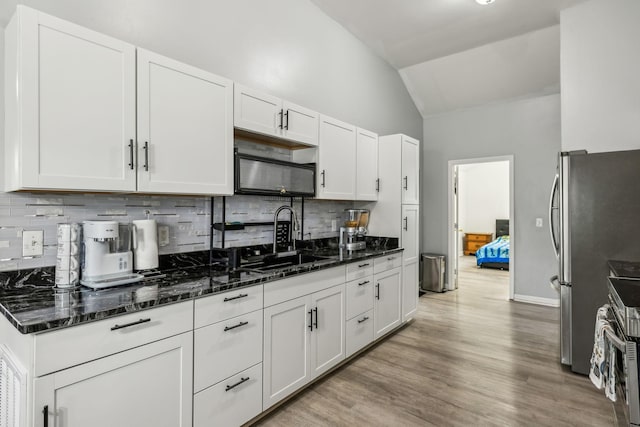 kitchen with a sink, appliances with stainless steel finishes, lofted ceiling, white cabinets, and backsplash