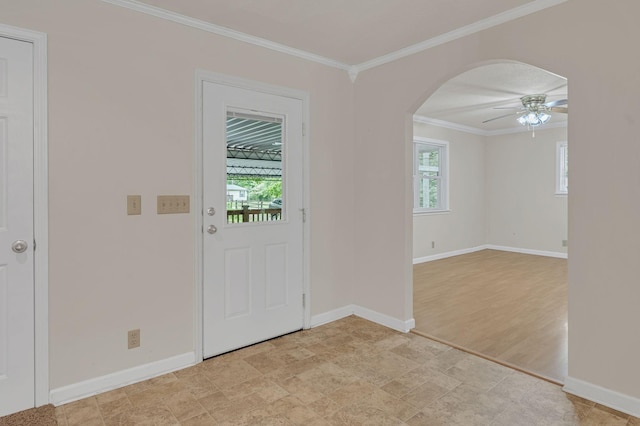 foyer featuring plenty of natural light, ornamental molding, arched walkways, ceiling fan, and baseboards
