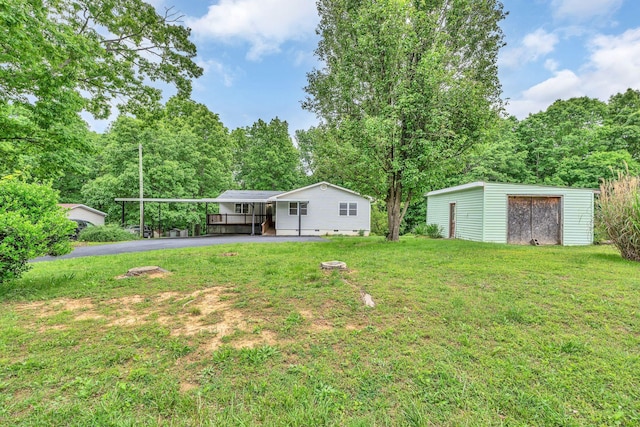 view of grassy yard with driveway, a carport, and an outdoor structure
