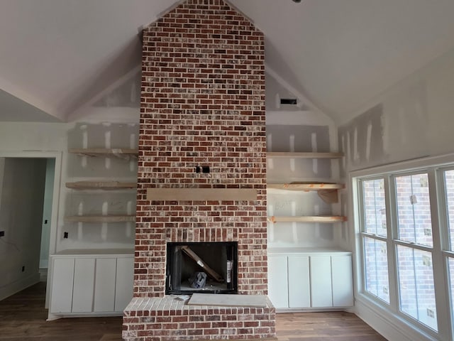 unfurnished living room with wood finished floors, a brick fireplace, and high vaulted ceiling