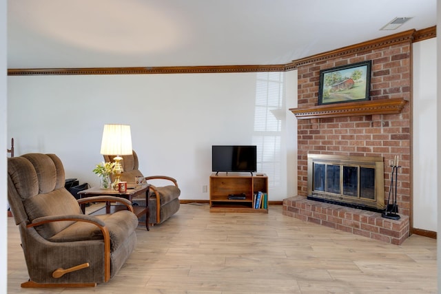 living area with wood finished floors, baseboards, a brick fireplace, and crown molding