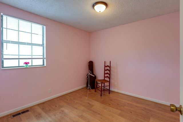 unfurnished room with light wood-style flooring, baseboards, and a textured ceiling