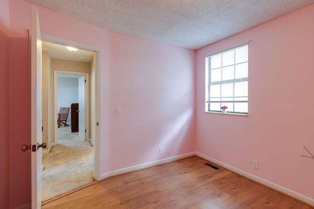 empty room featuring light wood-style floors, baseboards, and a textured ceiling