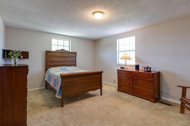 bedroom with multiple windows, light colored carpet, baseboards, and a textured ceiling