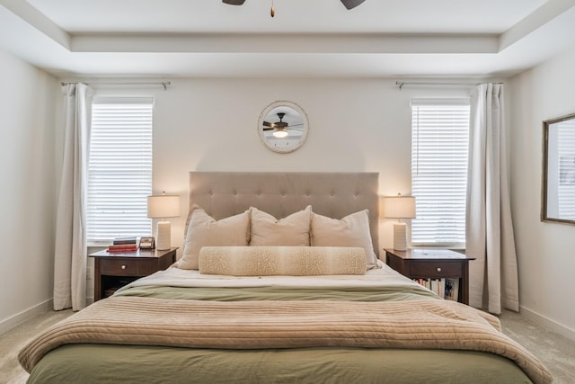 bedroom with light colored carpet, baseboards, multiple windows, and a raised ceiling