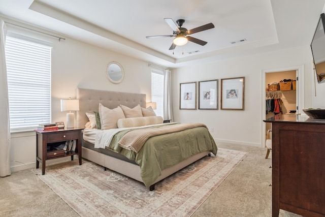bedroom with a raised ceiling, light colored carpet, a spacious closet, and baseboards