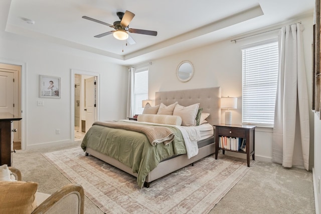 bedroom featuring a tray ceiling, carpet flooring, baseboards, and connected bathroom