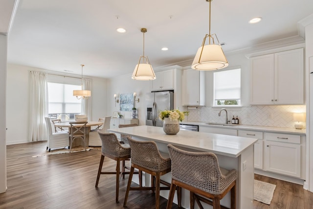 kitchen with stainless steel refrigerator with ice dispenser, a sink, backsplash, a kitchen island, and white cabinets