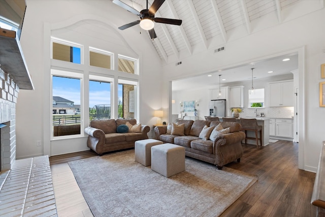 living room featuring ceiling fan, dark wood-style floors, a brick fireplace, high vaulted ceiling, and beam ceiling
