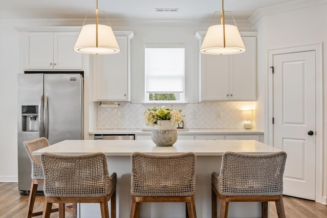 kitchen featuring stainless steel fridge, light wood finished floors, tasteful backsplash, light countertops, and crown molding