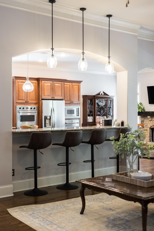109 Allenhurst Cir, Franklin, TN 37067 - kitchen featuring appliances with stainless steel finishes, ornamental molding, brown cabinetry, a kitchen bar, and stone countertops