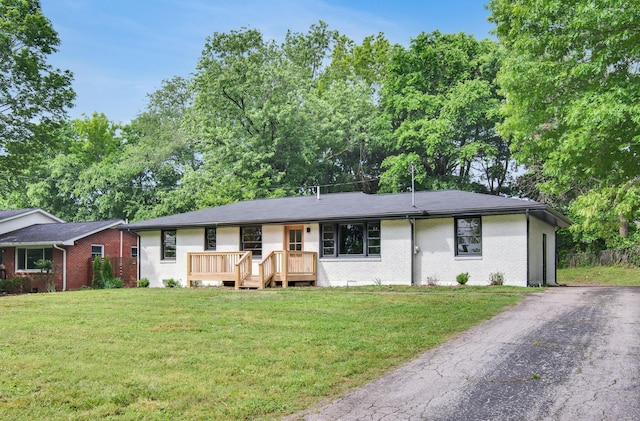 ranch-style home featuring a front lawn, brick siding, a wooden deck, and asphalt driveway