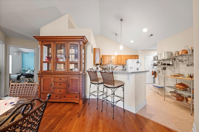 kitchen with white refrigerator with ice dispenser, a peninsula, lofted ceiling, a breakfast bar, and pendant lighting
