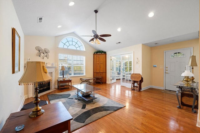 living room with a ceiling fan, healthy amount of natural light, vaulted ceiling, a fireplace with flush hearth, and light wood finished floors