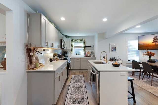 kitchen with a sink, stainless steel appliances, wood finished floors, a breakfast bar, and a kitchen island with sink