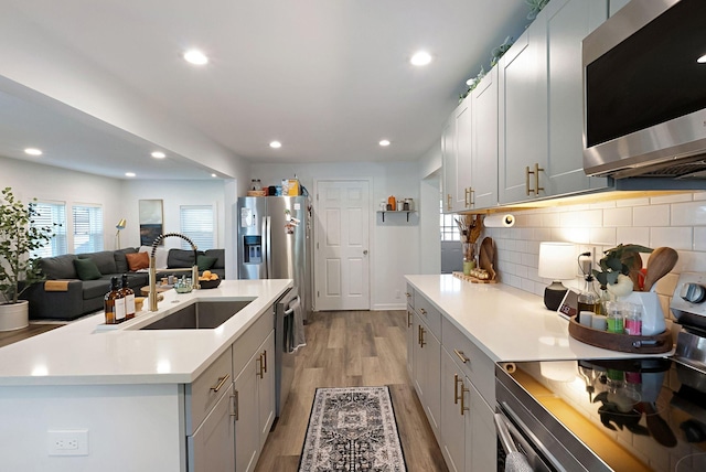 kitchen featuring appliances with stainless steel finishes, a sink, light countertops, light wood finished floors, and decorative backsplash