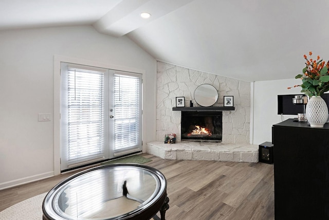 living area featuring lofted ceiling, french doors, wood finished floors, a stone fireplace, and baseboards