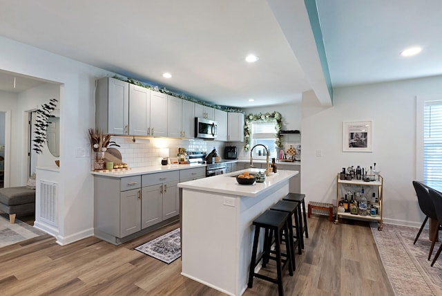 kitchen featuring stainless steel appliances, a sink, gray cabinets, a breakfast bar area, and light wood-style floors