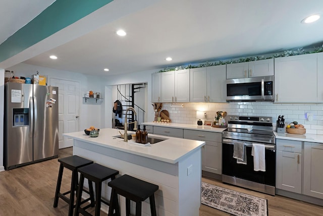 kitchen featuring appliances with stainless steel finishes, a sink, gray cabinetry, wood finished floors, and light countertops