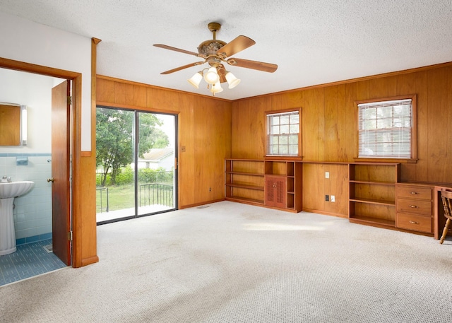 empty room featuring wood walls, carpet flooring, ceiling fan, a textured ceiling, and a sink