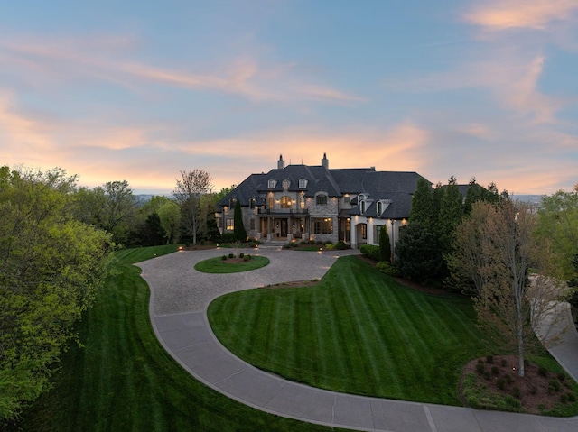 513 King Richards Ct, Franklin, TN 37067 - back of property at dusk featuring curved driveway, a balcony, a lawn, a chimney, and stone siding