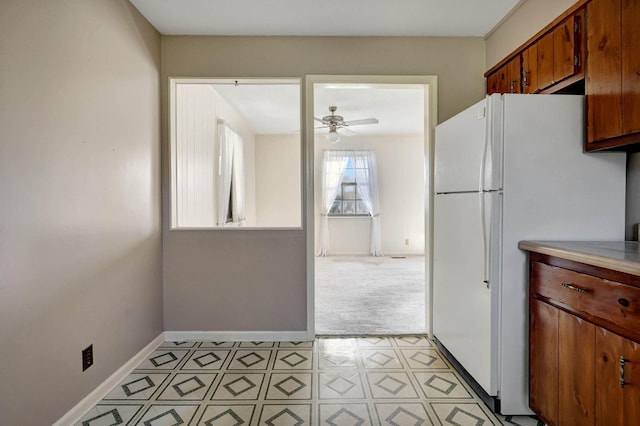 kitchen featuring freestanding refrigerator, ceiling fan, baseboards, brown cabinetry, and light countertops