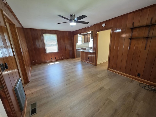 unfurnished living room with ceiling fan, light wood-style flooring, wooden walls, baseboards, and a sink