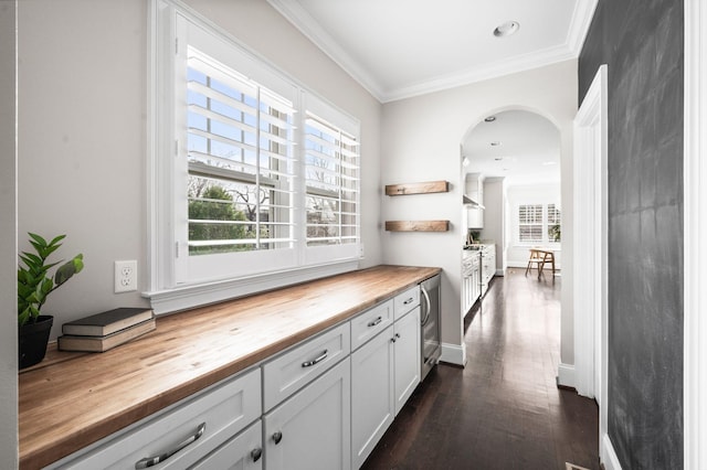hall with healthy amount of natural light, arched walkways, ornamental molding, beverage cooler, and dark wood finished floors
