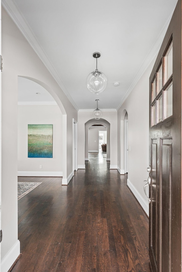 hall with arched walkways, dark wood finished floors, ornamental molding, and baseboards