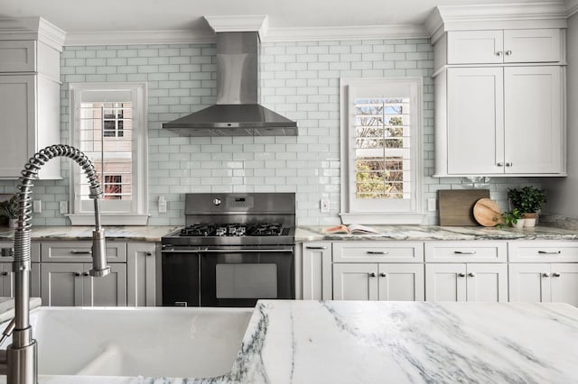 kitchen featuring range with gas cooktop, wall chimney range hood, ornamental molding, decorative backsplash, and white cabinets