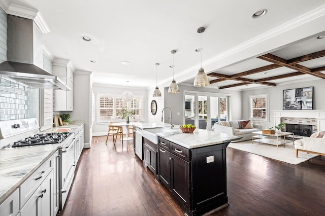 kitchen featuring gas stove, wall chimney range hood, a sink, dark wood-type flooring, and beam ceiling