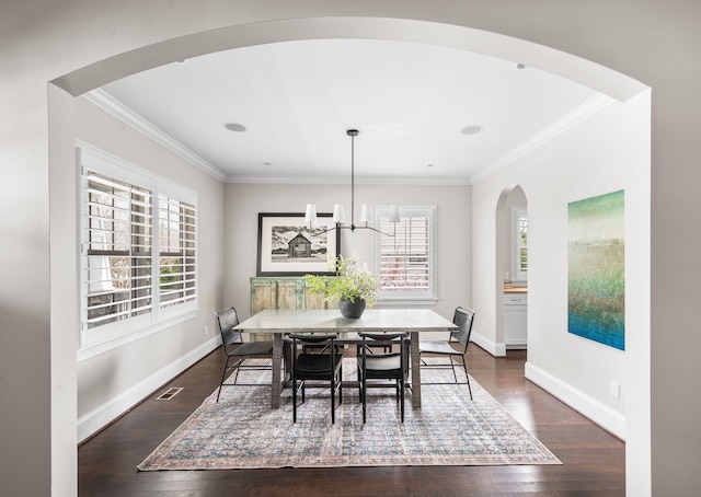 dining space featuring crown molding, arched walkways, a chandelier, dark wood-style flooring, and baseboards