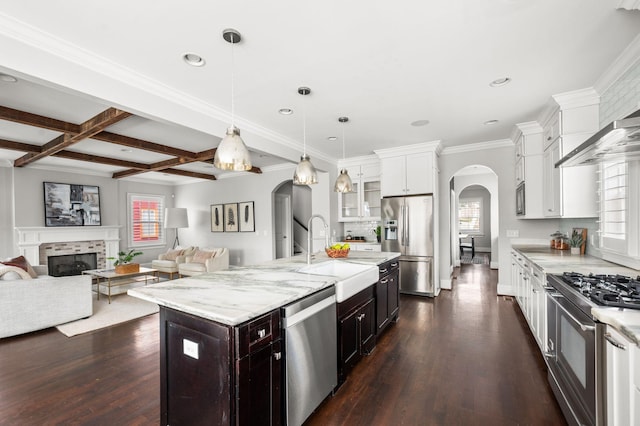 kitchen with arched walkways, appliances with stainless steel finishes, a sink, healthy amount of natural light, and beamed ceiling