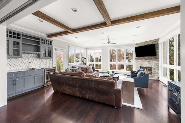 living area with beverage cooler, bar with sink, a fireplace, dark wood-style floors, and beam ceiling