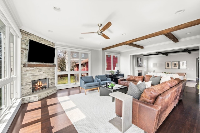 living room with a stone fireplace, ceiling fan, wood finished floors, beam ceiling, and ornamental molding