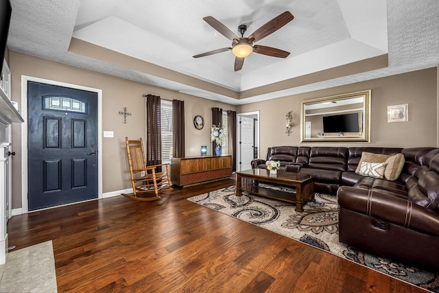 living area with a raised ceiling, ceiling fan, wood finished floors, and baseboards