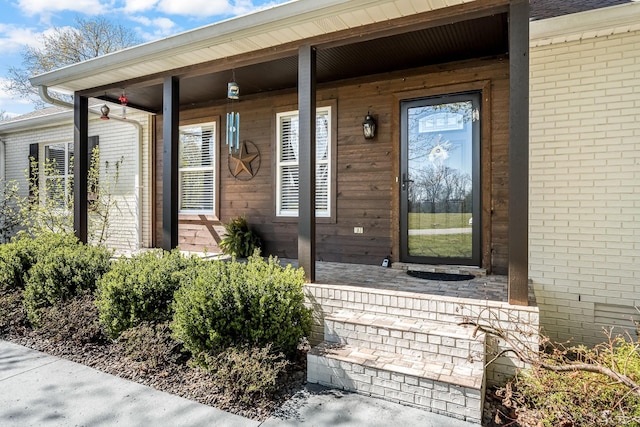 entrance to property with a porch and brick siding