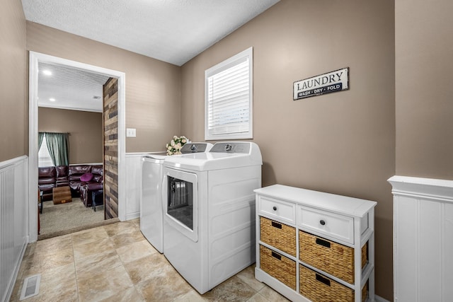 clothes washing area featuring independent washer and dryer, a wainscoted wall, a textured ceiling, and light colored carpet