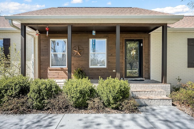 entrance to property with covered porch, roof with shingles, and brick siding