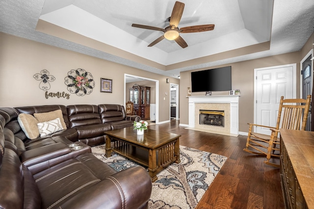 living room with a raised ceiling, a ceiling fan, baseboards, wood finished floors, and a fireplace