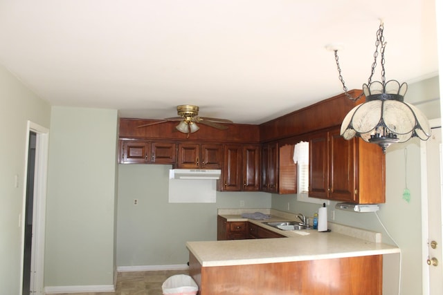 kitchen with a sink, under cabinet range hood, light countertops, and a peninsula